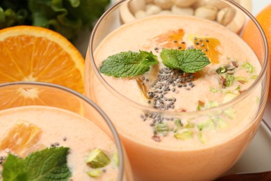 Photo of Superfood. Tasty smoothie with chia seeds, mint, pistachio and orange in glasses on white table, closeup