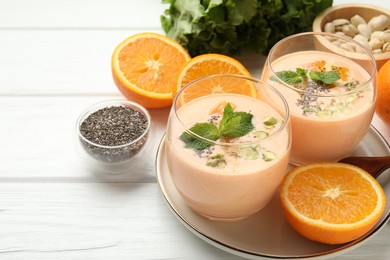 Photo of Superfood. Tasty smoothie with chia seeds, mint, pistachio and oranges on white wooden table, closeup