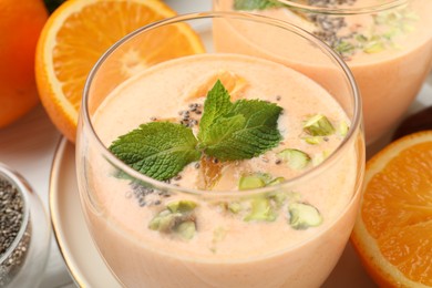 Photo of Superfood. Tasty smoothie with chia seeds, mint, pistachio and orange in glass on white table, closeup