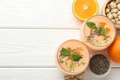 Photo of Superfood. Tasty smoothie with chia seeds, mint, pistachio and oranges on white wooden table, flat lay. Space for text