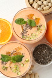 Photo of Superfood. Tasty smoothie with chia seeds, mint, pistachio and oranges on white wooden table, flat lay