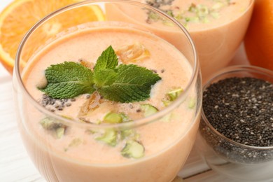 Photo of Superfood. Tasty smoothie with chia seeds, mint, pistachio and orange in glasses on white wooden table, closeup