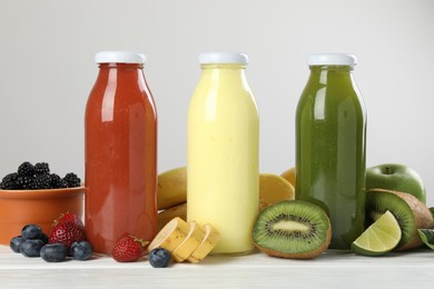Photo of Superfood. Bottles with tasty smoothies and ingredients on white wooden table, closeup