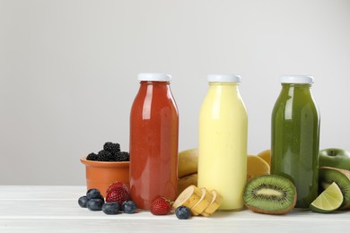 Photo of Superfood. Bottles with tasty smoothies and ingredients on white wooden table against light grey background, closeup