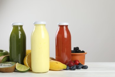 Photo of Superfood. Bottles with tasty smoothies and ingredients on white wooden table against light grey background, closeup