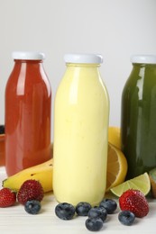 Photo of Superfood. Bottles with tasty smoothies and ingredients on white wooden table, closeup