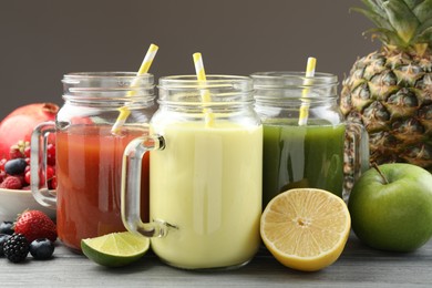 Photo of Superfood. Tasty smoothies in mason jars and ingredients on wooden table against grey background, closeup