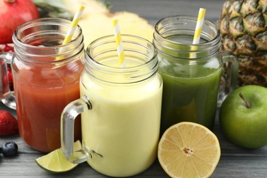 Photo of Superfood. Tasty smoothies in mason jars and ingredients on grey wooden table, closeup