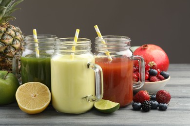 Photo of Superfood. Tasty smoothies in mason jars and ingredients on wooden table against grey background, closeup
