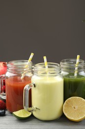 Photo of Superfood. Tasty smoothies in mason jars and ingredients on wooden table against grey background, closeup