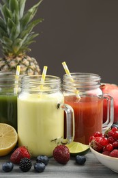 Photo of Superfood. Tasty smoothies in mason jars and ingredients on wooden table against grey background, closeup