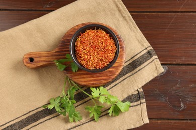 Photo of Saffron in bowl and coriander on wooden table, flat lay. Aromatic spices