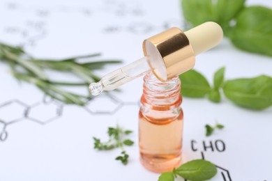 Photo of Different herbs and bottle of cosmetic product on paper with chemical formulas, closeup