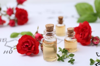 Photo of Bottles of cosmetic products, herbs and red roses on paper with chemical formulas, closeup