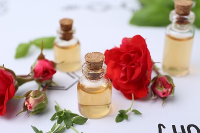Photo of Bottles of cosmetic products, herbs and red roses on paper with chemical formulas, closeup