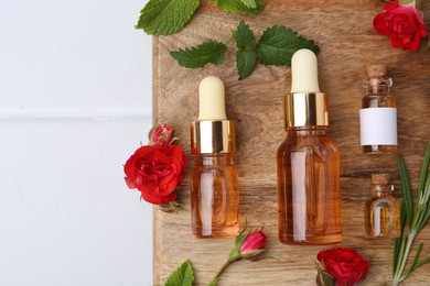Photo of Bottles of essential oils, red roses and herbs on white table, flat lay