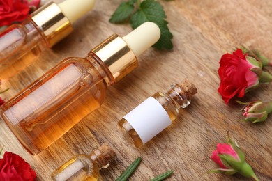 Photo of Bottles of essential oils, red roses and herbs on wooden table, closeup
