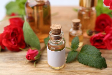 Photo of Bottles of essential oils, red roses and herbs on wooden table, closeup