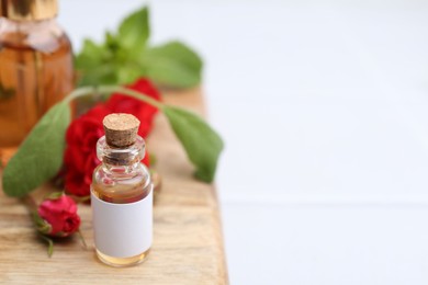 Photo of Bottles of essential oils, red roses and herbs on table, closeup. Space for text