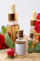 Photo of Bottles of essential oils, red roses and herbs on wooden table, closeup