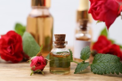 Photo of Bottles of essential oils, red roses and herbs on wooden table, closeup