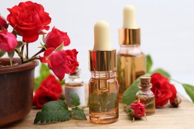 Photo of Bottles of essential oils, red roses and herbs on wooden table, closeup