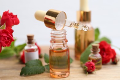Photo of Bottles of essential oils, red roses and herbs on wooden table, closeup