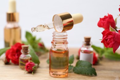 Photo of Bottles of essential oils, red roses and herbs on wooden table, closeup
