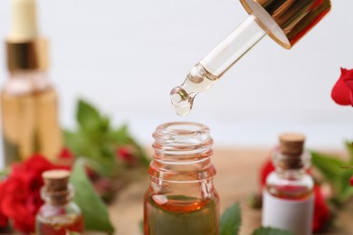 Photo of Dripping essential oil into bottle on blurred background, closeup