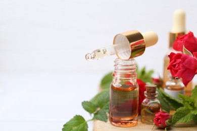 Photo of Bottles of essential oils, red roses and herbs on table, closeup. Space for text
