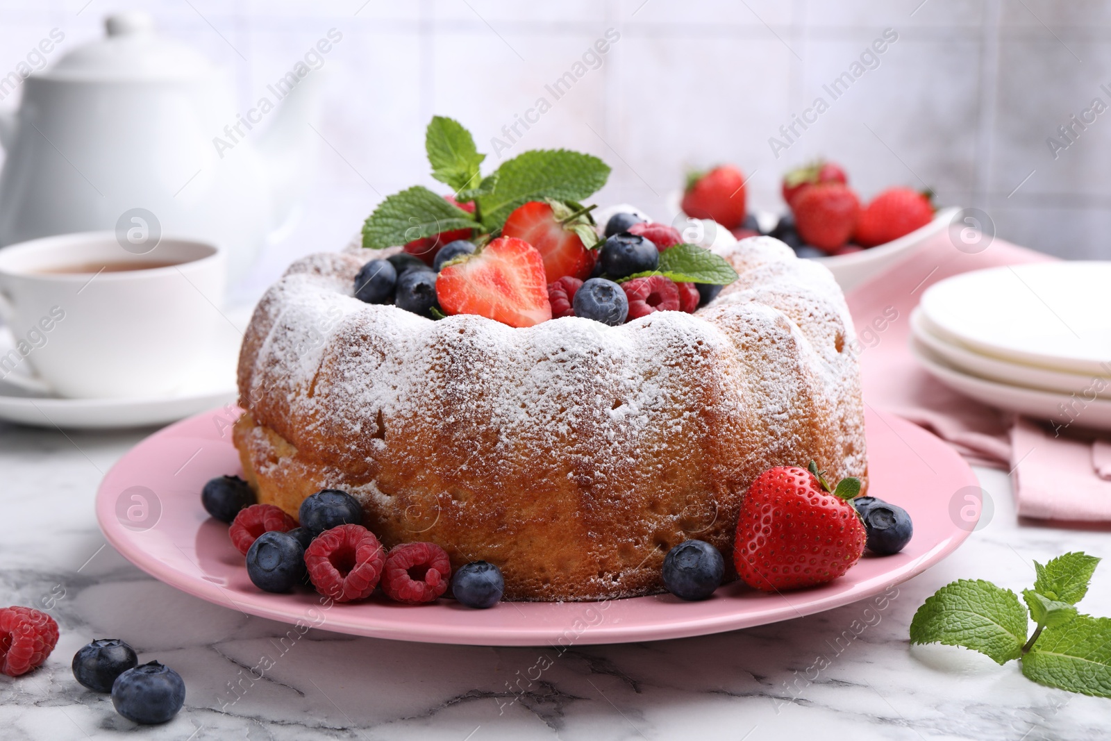 Tasty Bundt cake with powdered sugar and berries on white marble table, closeup Photo of Tasty Bundt cake with powdered sugar and berries on white marble table, closeup