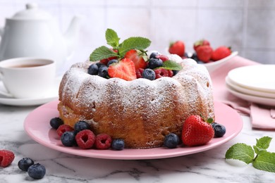 Photo of Tasty Bundt cake with powdered sugar and berries on white marble table, closeup