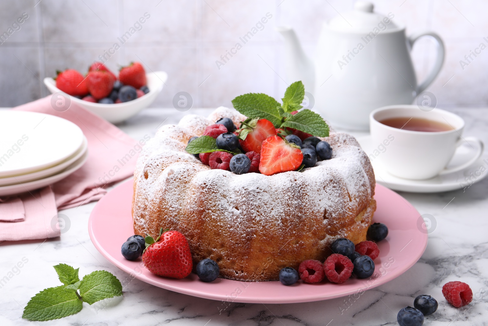 Tasty Bundt cake with powdered sugar and berries on white marble table, closeup Photo of Tasty Bundt cake with powdered sugar and berries on white marble table, closeup