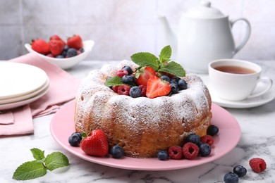 Photo of Tasty Bundt cake with powdered sugar and berries on white marble table, closeup