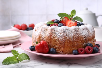 Photo of Tasty Bundt cake with powdered sugar and berries on white marble table, closeup
