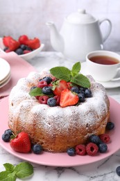 Photo of Tasty Bundt cake with powdered sugar and berries on white marble table, closeup