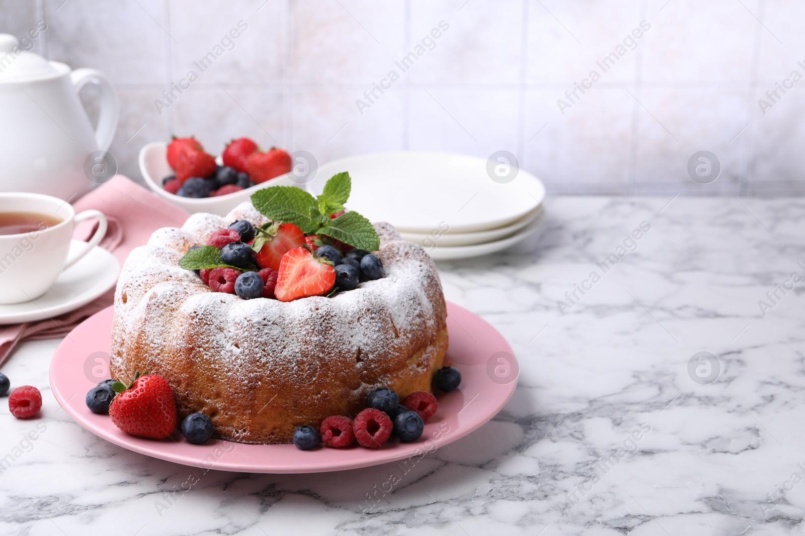 Tasty Bundt cake with powdered sugar and berries on white marble table, space for text Photo of Tasty Bundt cake with powdered sugar and berries on white marble table, space for text