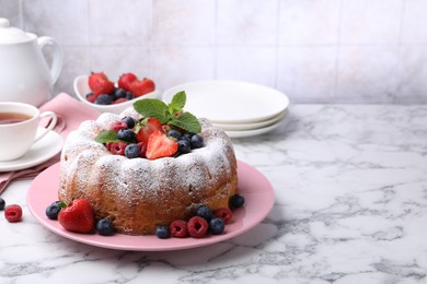 Photo of Tasty Bundt cake with powdered sugar and berries on white marble table, space for text