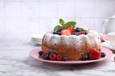 Photo of Tasty Bundt cake with powdered sugar and berries on white marble table, closeup. Space for text