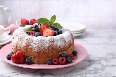 Photo of Tasty Bundt cake with powdered sugar and berries on white marble table, closeup. Space for text