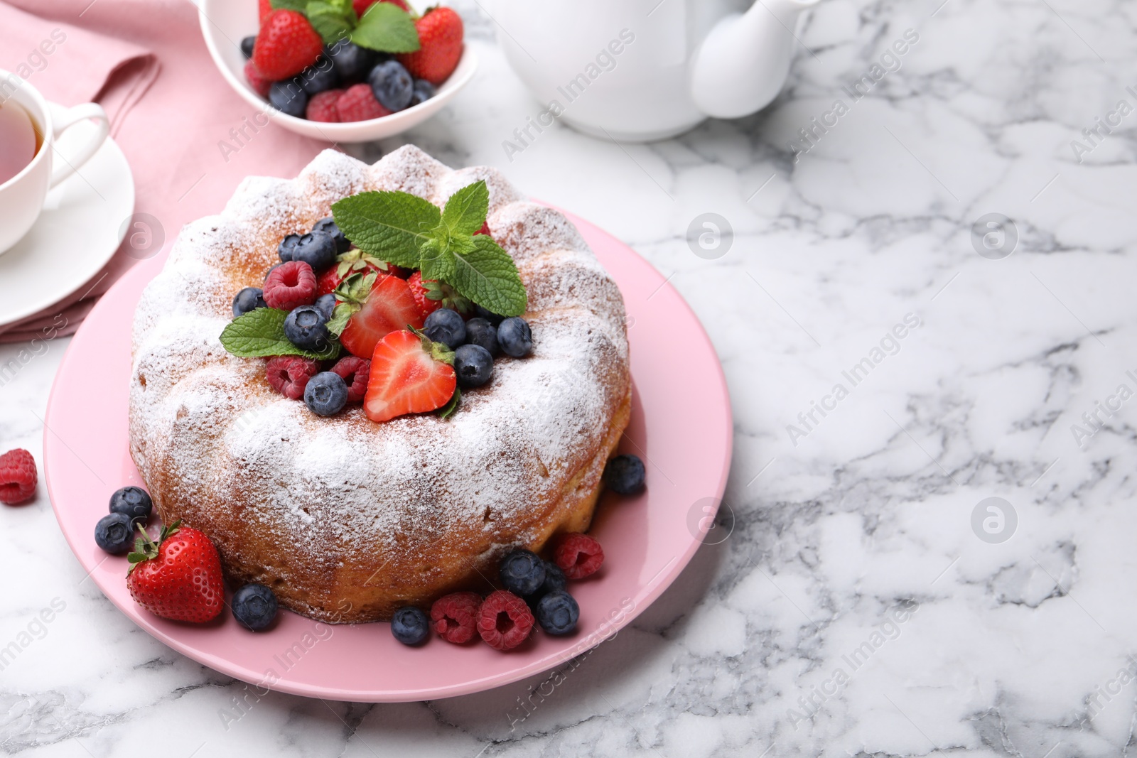 Tasty Bundt cake with powdered sugar and berries on white marble table, space for text Photo of Tasty Bundt cake with powdered sugar and berries on white marble table, space for text