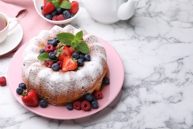 Photo of Tasty Bundt cake with powdered sugar and berries on white marble table, space for text