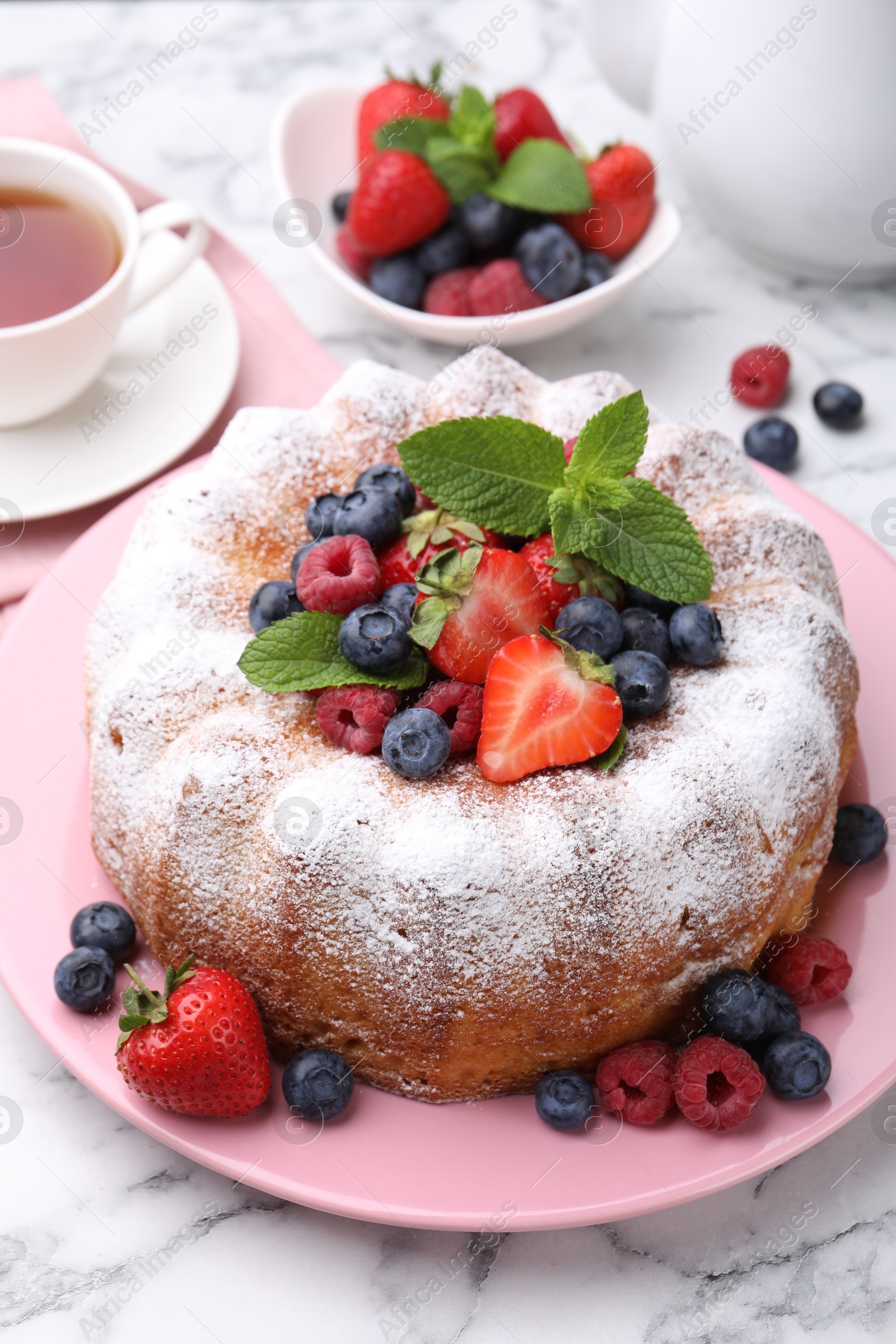 Tasty Bundt cake with powdered sugar and berries on white marble table, closeup Photo of Tasty Bundt cake with powdered sugar and berries on white marble table, closeup