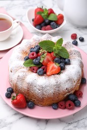 Photo of Tasty Bundt cake with powdered sugar and berries on white marble table, closeup