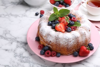 Photo of Tasty Bundt cake with powdered sugar and berries on white marble table, closeup. Space for text