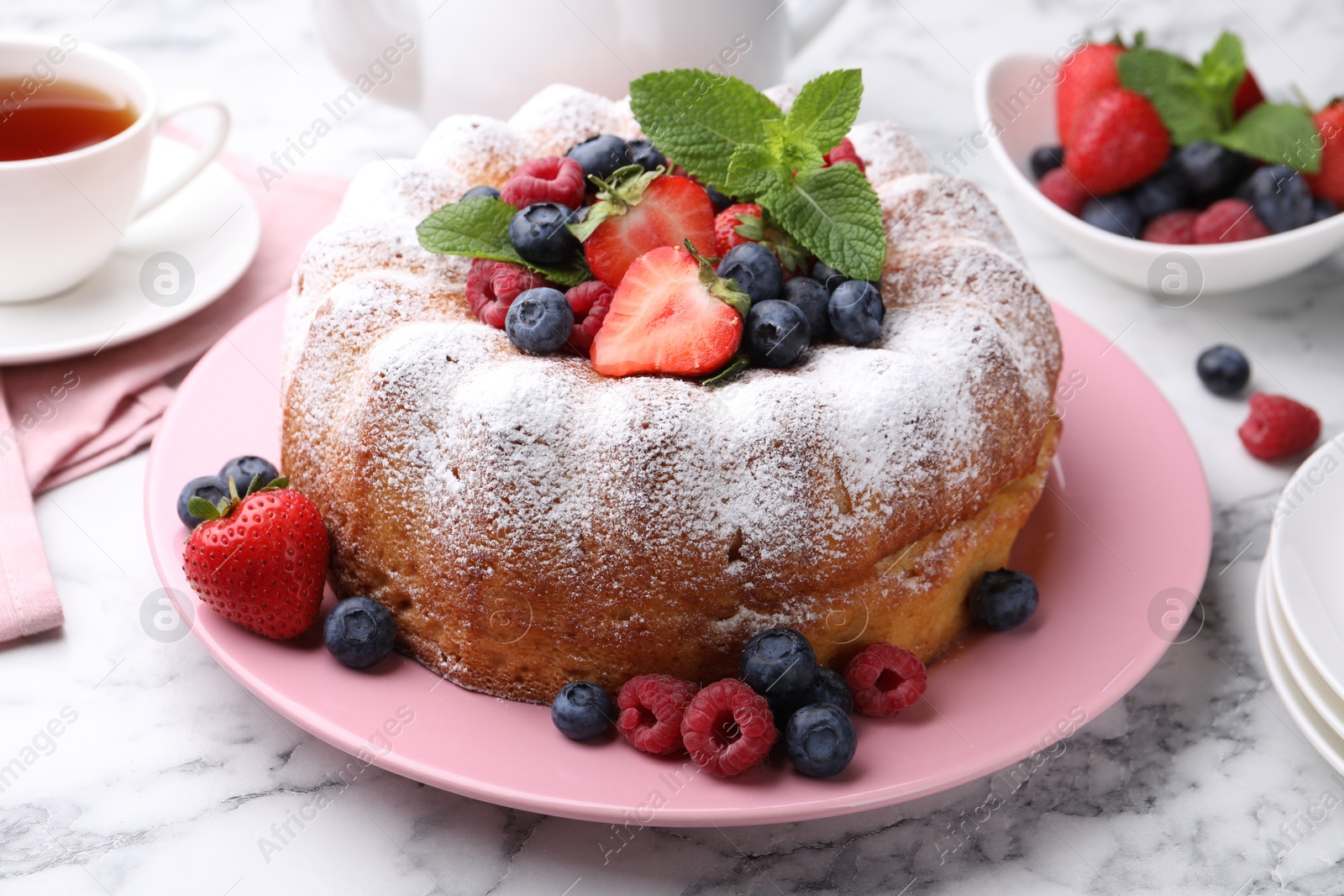 Tasty Bundt cake with powdered sugar and berries on white marble table, closeup Photo of Tasty Bundt cake with powdered sugar and berries on white marble table, closeup