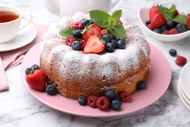 Photo of Tasty Bundt cake with powdered sugar and berries on white marble table, closeup