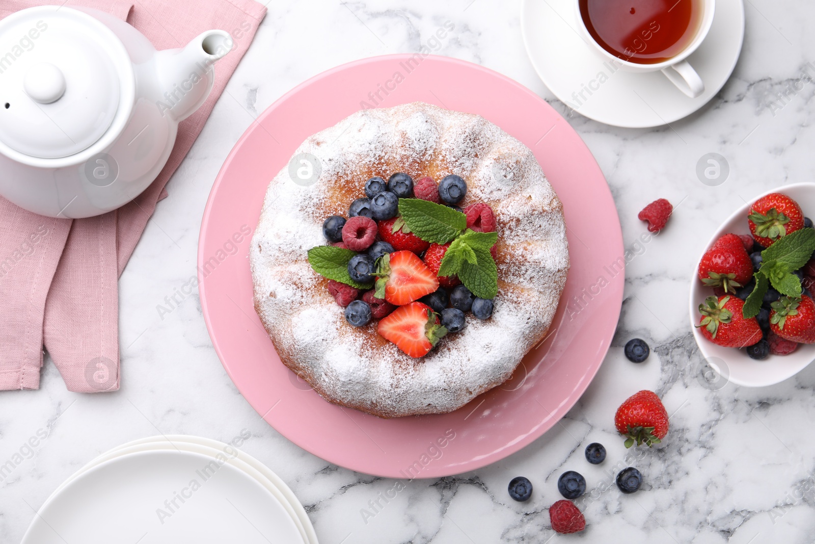 Tasty Bundt cake with powdered sugar and berries on white marble table, flat lay Photo of Tasty Bundt cake with powdered sugar and berries on white marble table, flat lay