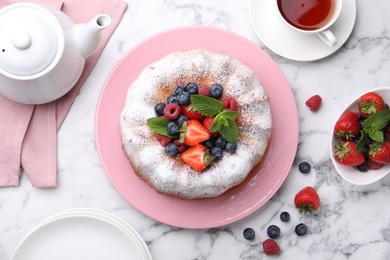 Photo of Tasty Bundt cake with powdered sugar and berries on white marble table, flat lay