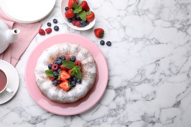 Photo of Tasty Bundt cake with powdered sugar and berries on white marble table, flat lay. Space for text